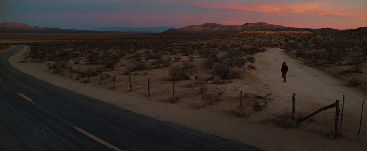 Nocturnal Animals (2016) movie still: wide — A vast, barren desert landscape stretches out beneath a colorful dusk sky. A lone man walks away on a…