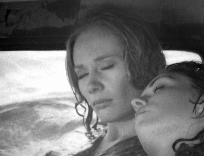 Carnival of Souls (1962) movie still: closeup — The interior of a car features bright light filtering through a side window. Two women lean against…
