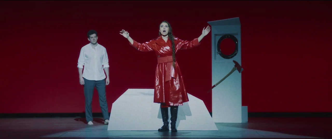 She Came To Me (2023) movie still: fullbody — A theatrical stage with a flat red background and minimalist white geometric set pieces. A woman…