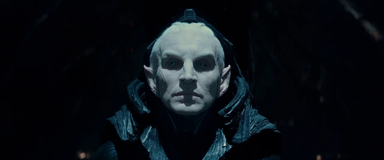 Thor: The Dark World (2013) movie still: closeup — A dimly lit, shadowed space with minimal architectural detail visible. An elf-like humanoid…