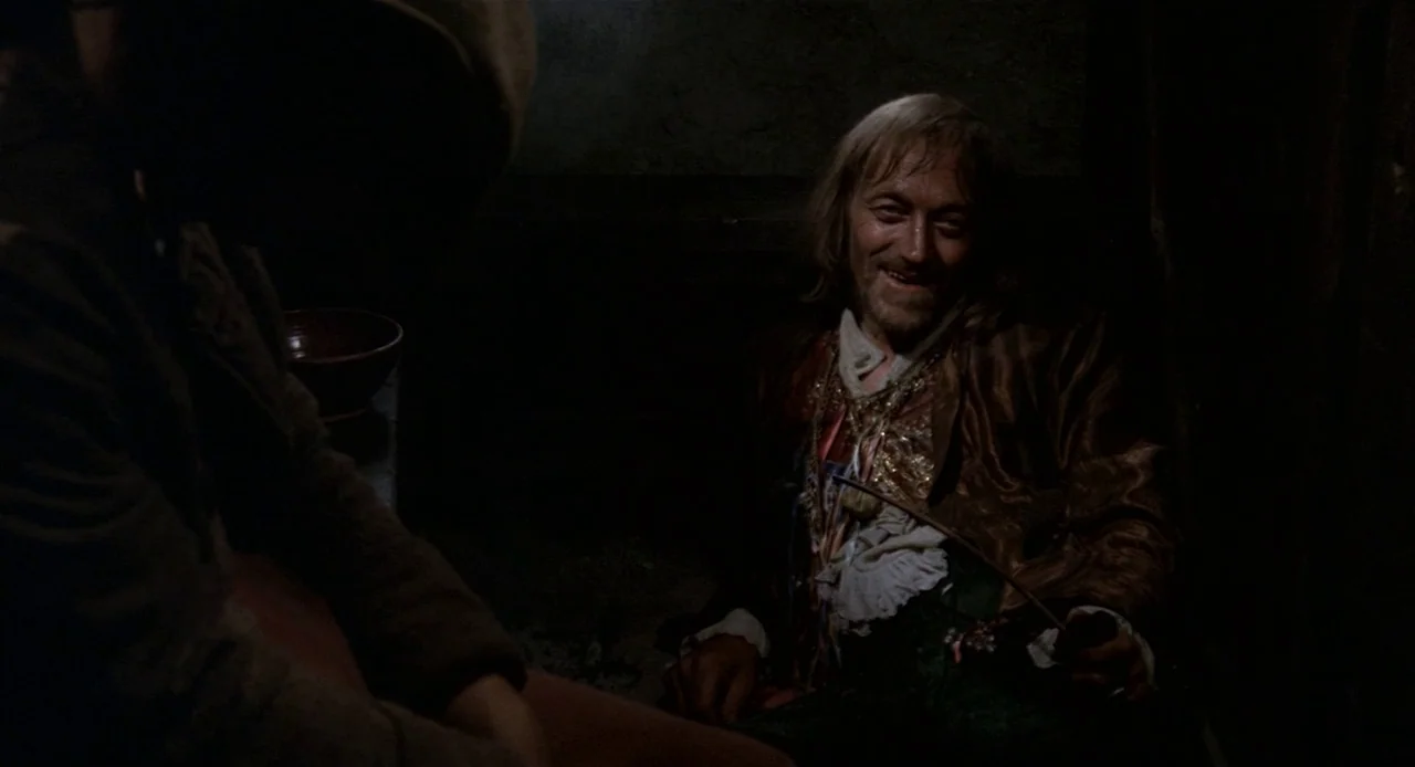 Fellini’s Casanova (1976) movie still: medium — A dark stone cell contains a man in a velvet jacket holding a pipe. The man sits while facing…