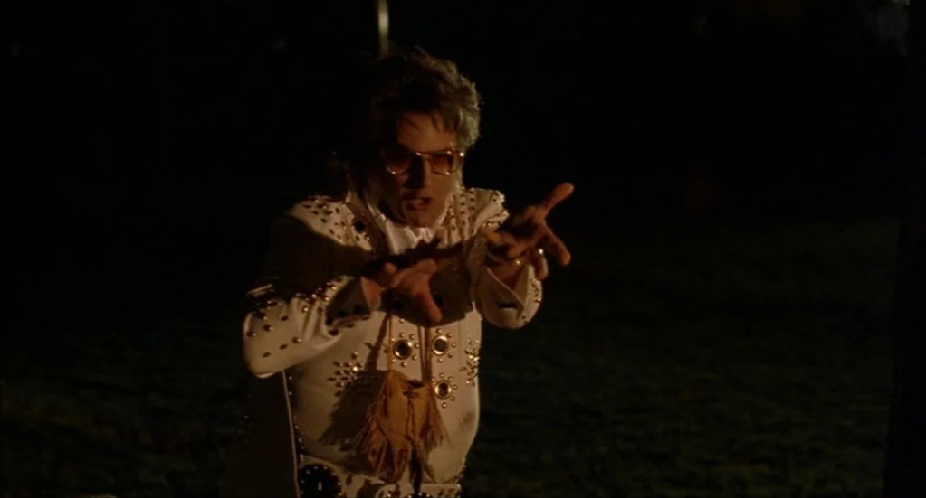 Bubba Ho-Tep (2002) movie still: medium — An impersonator stands in a dark outdoor environment at night. The man in an Elvis costume extends his…