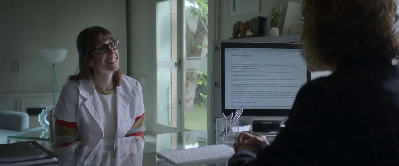 Crazy About Her (2021) movie still: medium — A light-filled office space features a glass desk and a large windowed door. A young woman in a white…