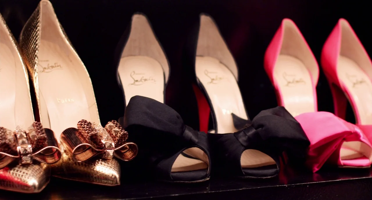 The Bling Ring (2013) movie still: closeup — A close-up of three pairs of high-heeled shoes lined up on a black shelf. Each pair of designer shoes…