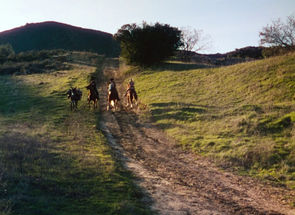 Calamity Jane (1953) movie still: wide — A dirt path cuts through a grassy, hilly landscape during late afternoon. Three people on horseback and one…