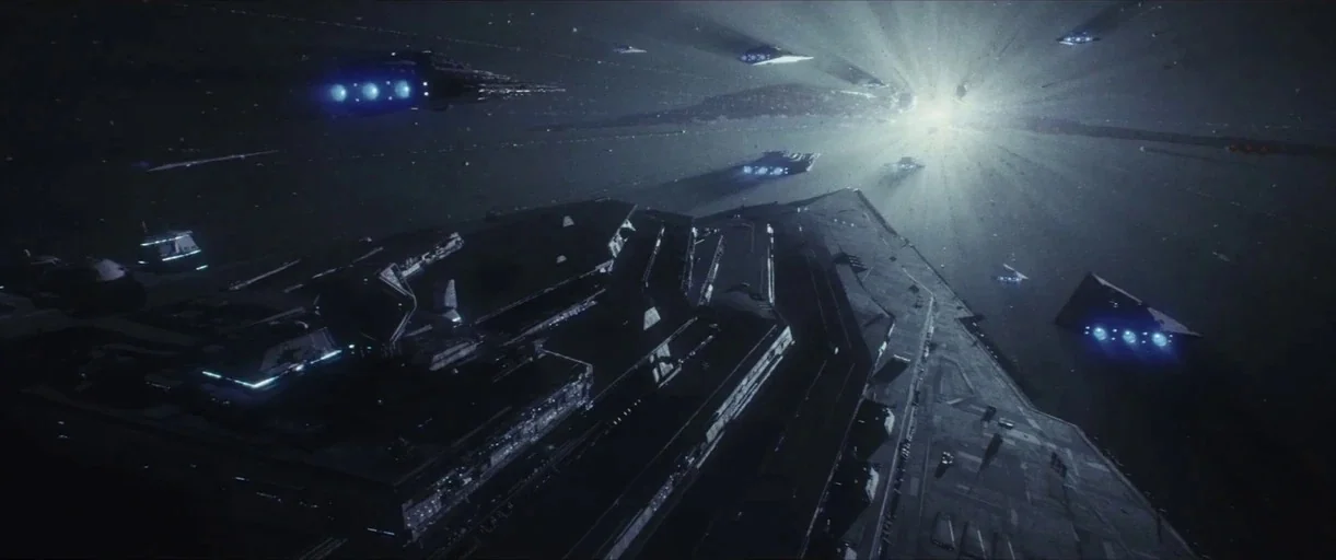 Star Wars: The Last Jedi (2017) movie still: establishing — An expanse of dark space filled with large, angular starships moving in formation. A…