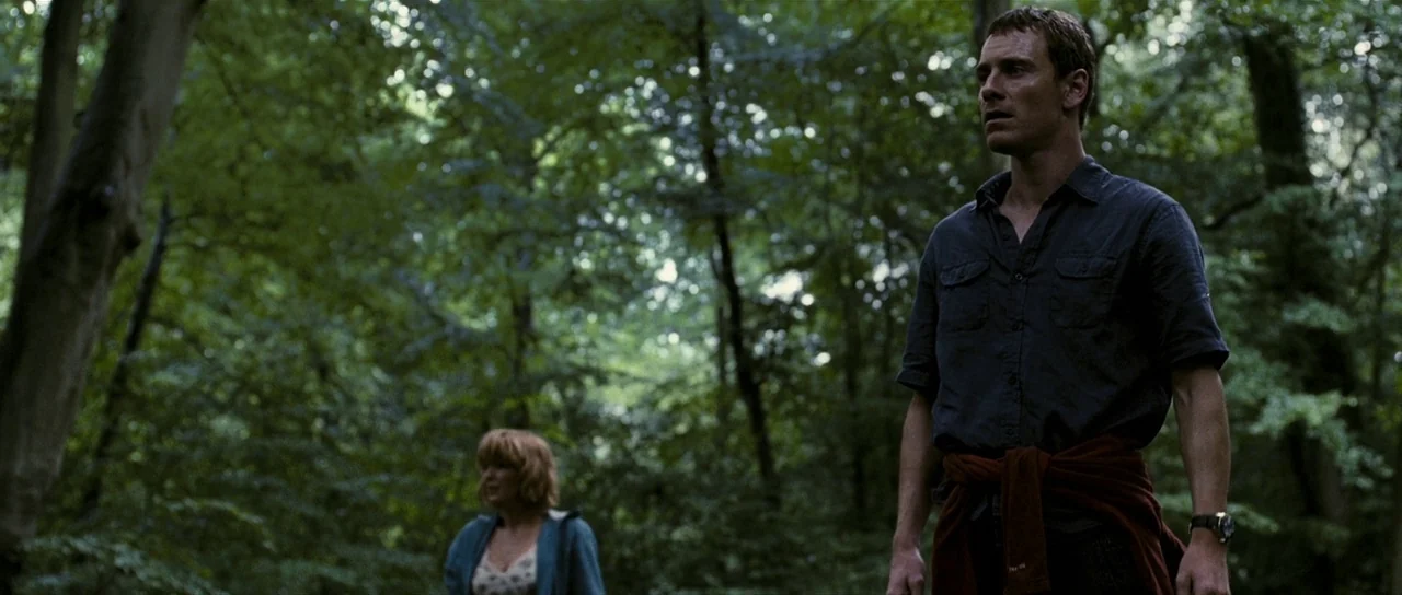 Eden Lake (2008) movie still: medium — A dense green forest with thick vegetation and tall trees filling the frame. A man stands in the foreground…