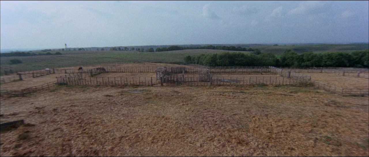 The Grand Duel (1972) movie still: establishing — An expanse of dry grassland features wooden corrals constructed with multiple fenced enclosures.…