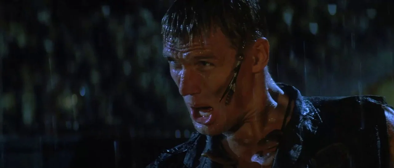 Universal Soldier (1992) movie still: closeup — A dark city street at night during a heavy rainstorm with blurred background lights. A muscular man…