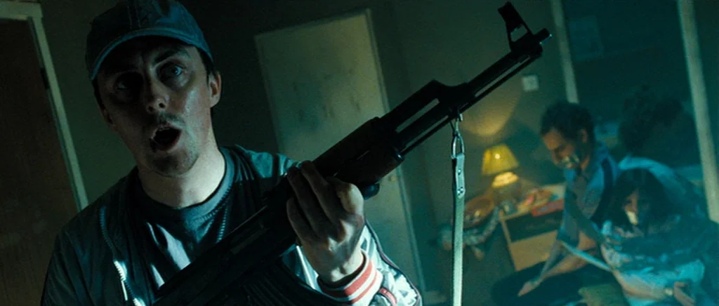 Hot Fuzz (2007) movie still: medium — A dimly lit room with blue ambient light features a man holding a rifle. Two other individuals are seated in…