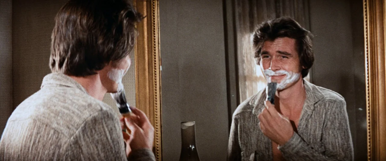 Westworld (1973) movie still: medium — A man stands before a large gold-framed mirror in a dimly lit indoor space. He is applying white shaving…