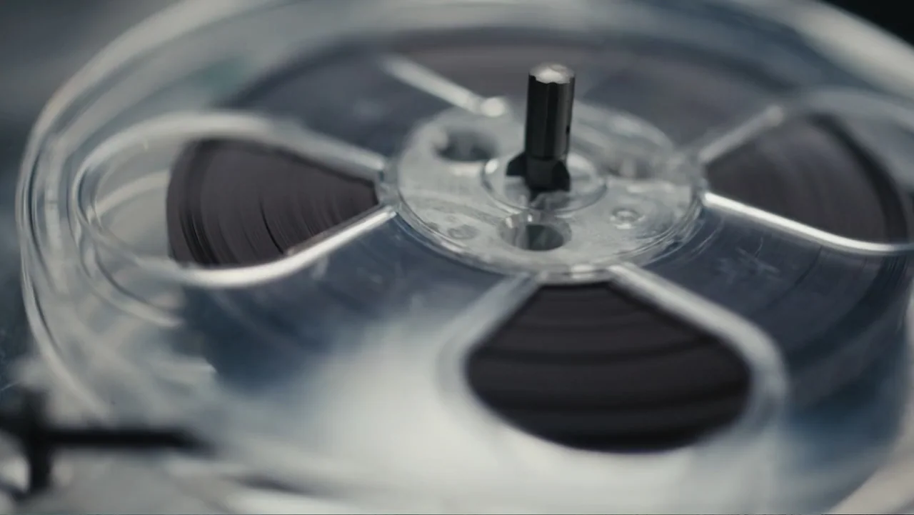 Elizabeth Taylor: The Lost Tapes (2024) movie still: closeup — A close-up view of a transparent plastic film reel mounted on a spindle. Dark film…