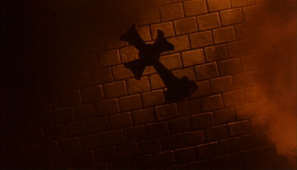 Bram Stoker’s Dracula (1992) movie still: closeup — A dark brick wall is illuminated by a warm, directional orange light. A silhouetted cross is…