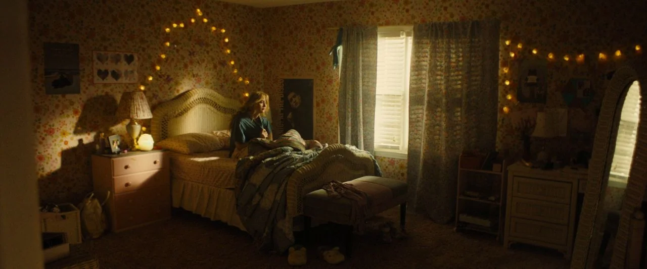 Freaky (2020) movie still: medium — A cluttered teen bedroom features floral wallpaper, a wicker bed frame, and string lights. A young woman sits…