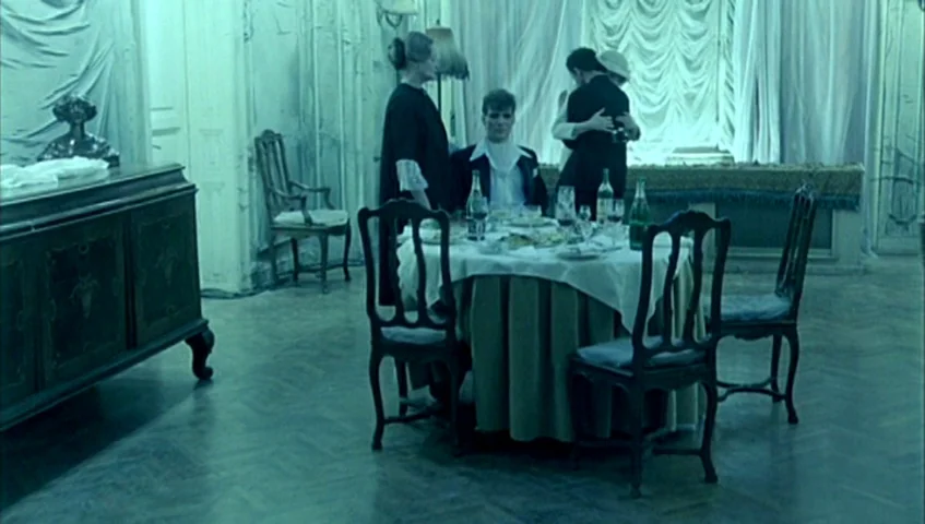 Almanac of Fall (1984) movie still: wide — A dimly lit room with covered furniture and draped curtains features a dining setup. People in formal…