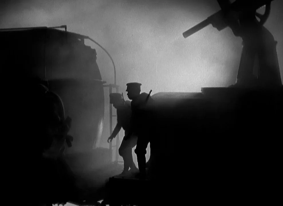 Shanghai Express (1932) movie still: fullbody — A dark, foggy rail yard at night features industrial train silhouettes. Two soldiers walk alongside…