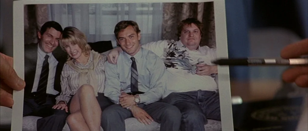 I Heart Huckabees (2004) movie still: closeup — A person holds a photograph of four individuals sitting together on a couch. The photograph captures…