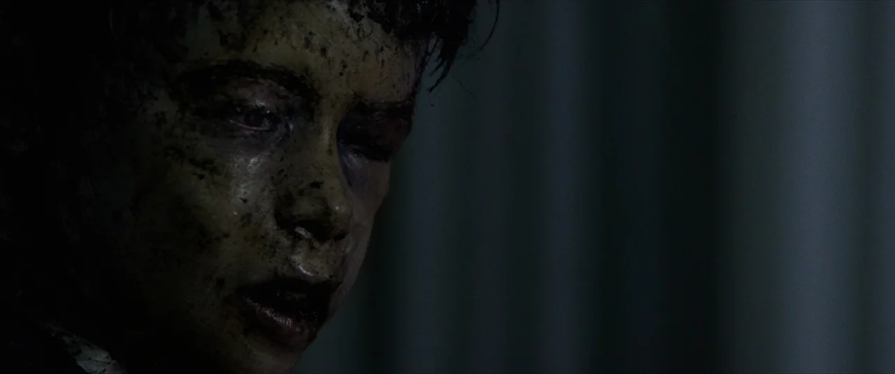 Terrified (2017) movie still: closeup — The scene is a dimly lit interior space with shadows dominating the background. A young person has a face…