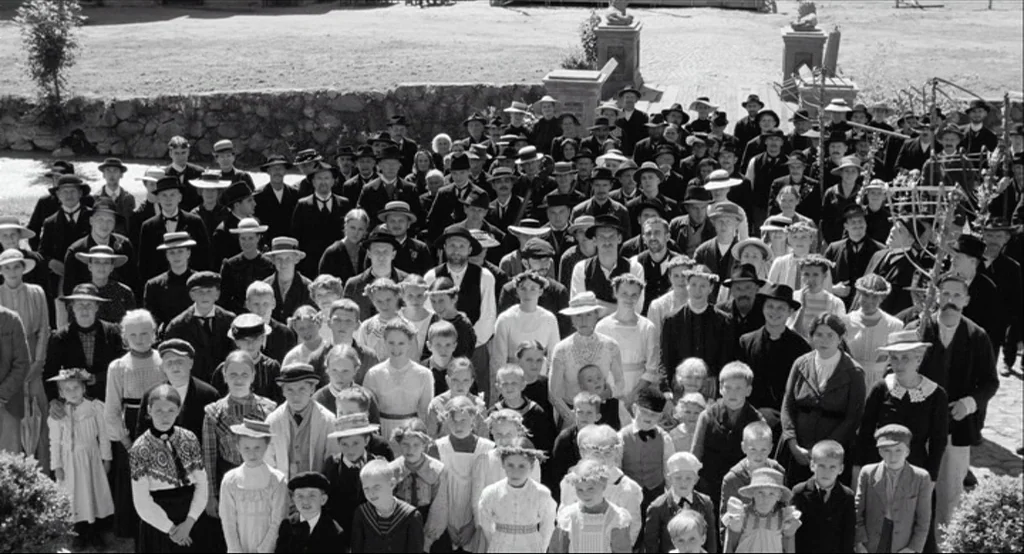 The White Ribbon (2009) movie still: wide — A large crowd of men, women, and children stand together in an outdoor courtyard. The group poses for a…