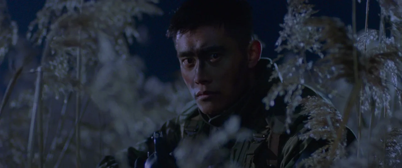 Joint Security Area (2000) movie still: medium — A man in military gear crouches among tall, dry reeds during the night. He stares directly ahead…