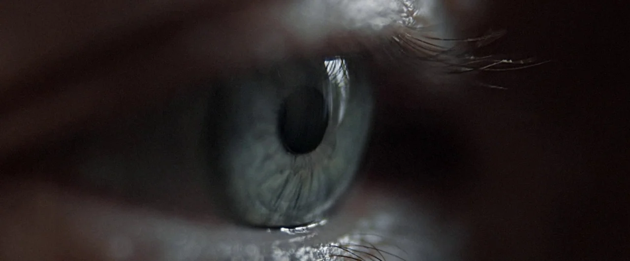 No Man of God (2021) movie still: closeup — An extreme close-up of a human eye shows the texture of the iris. The reflection of a bright light…