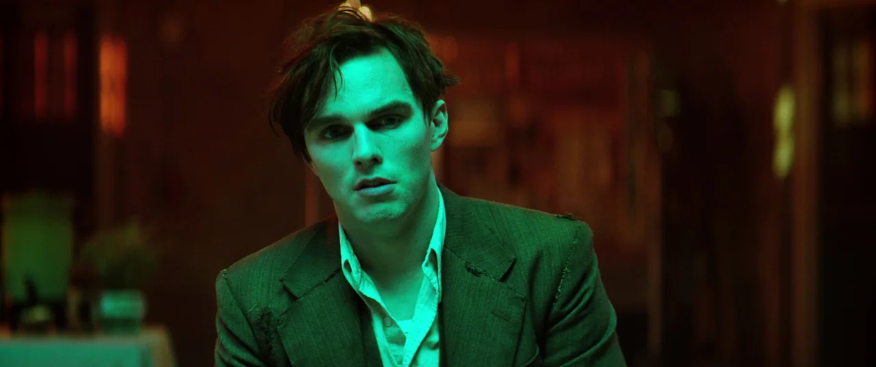 Renfield (2023) movie still: medium — A man stands in a dimly lit, dark space filled with deep green and red colors. The subject stares ahead with a…