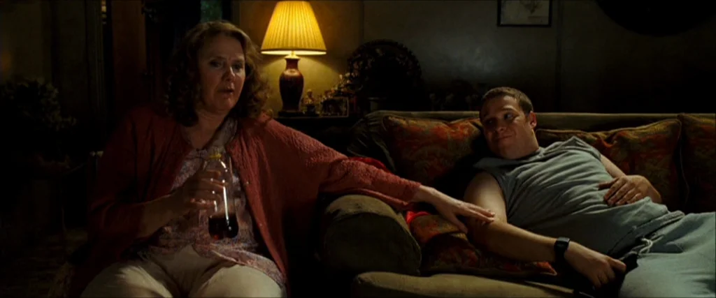 Observe And Report (2009) movie still: medium — A dimly lit room features a woman sitting on a sofa next to a man. The woman holds a brown plastic…
