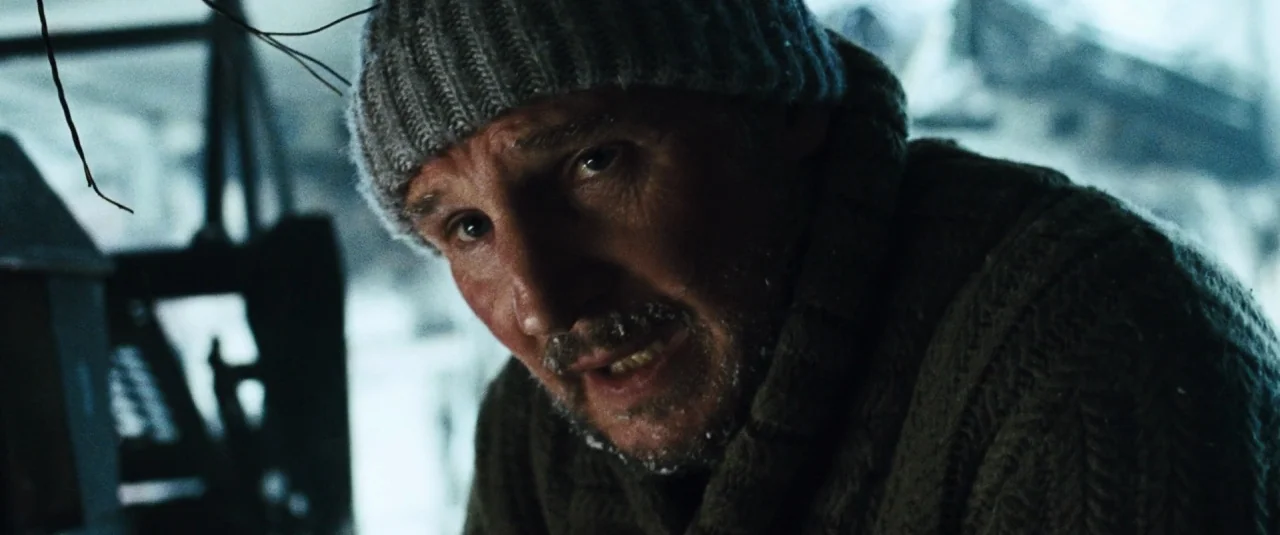 The Grey (2012) movie still: closeup — A snowy wilderness with blurred debris and white landscape in the background. A man with frost-covered facial…