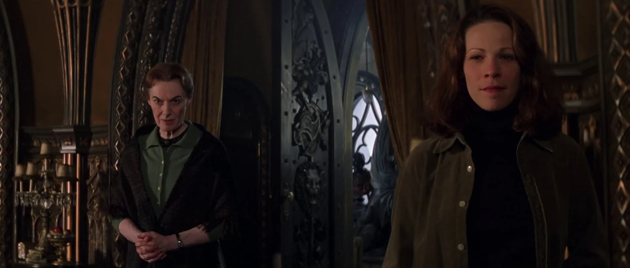 The Haunting (1999) movie still: medium — An interior space with elaborate wood carvings and dark paneling features a gothic aesthetic. Two women…