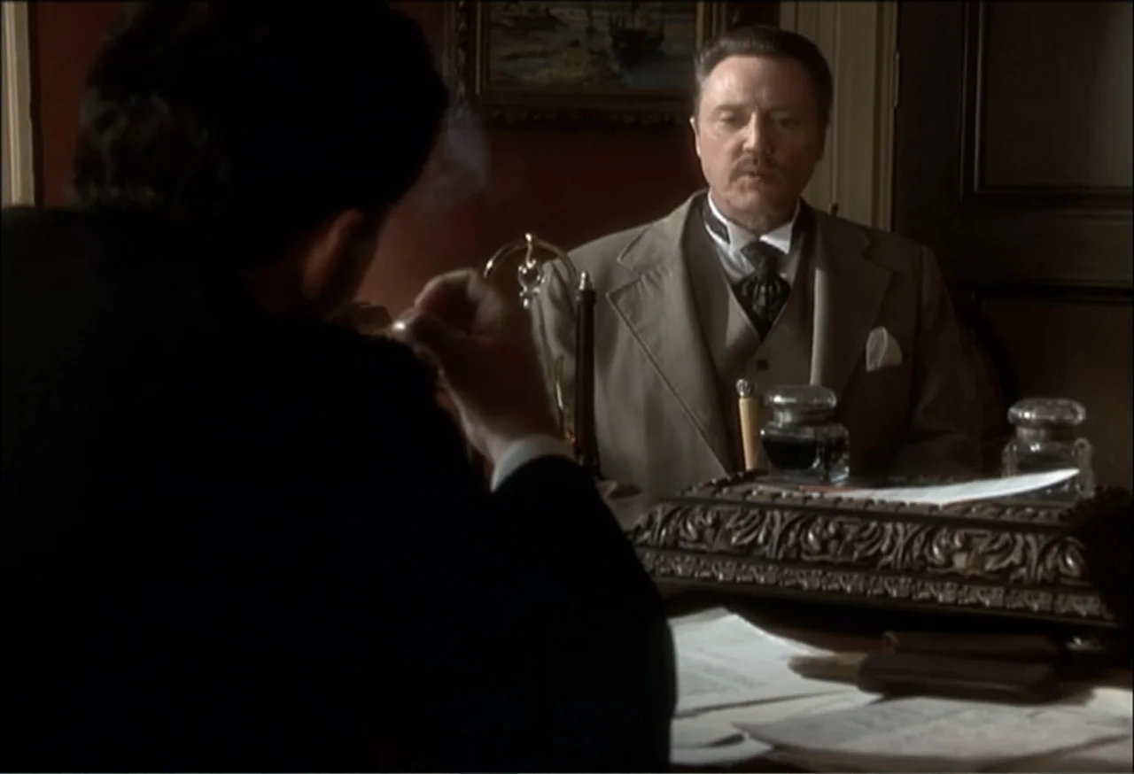 Vendetta (2022) movie still: medium — A wood-paneled room contains an ornate desk with inkwells and scattered documents. An older man in a tan suit…