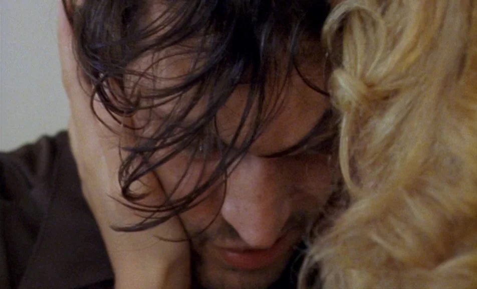 The Brown Bunny (2003) movie still: closeup — A close-up shot focuses on a man and woman leaning heads together. The man has messy dark hair and the…