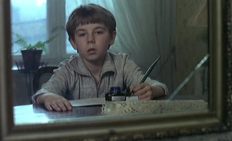 Blind Chance (1987) movie still: medium — A young boy sits at a table near a window in a dimly lit room. He holds a fountain pen in his right hand…