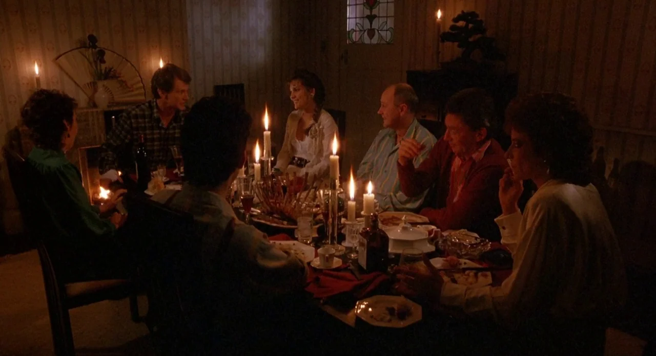 Hellraiser (1987) movie still: wide — A dimly lit dining room with striped wallpaper contains a crowded dinner table. Six adults sit around the…