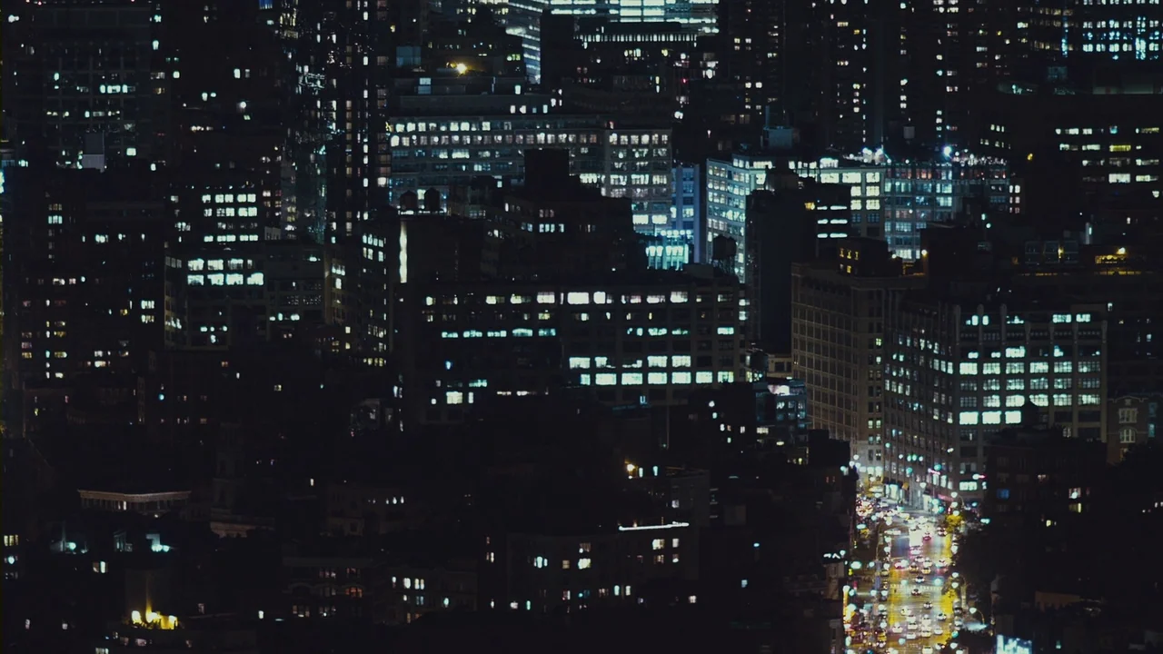 Margin Call (2011) movie still: establishing — A dense urban cityscape at night shows closely packed buildings with illuminated office windows.…