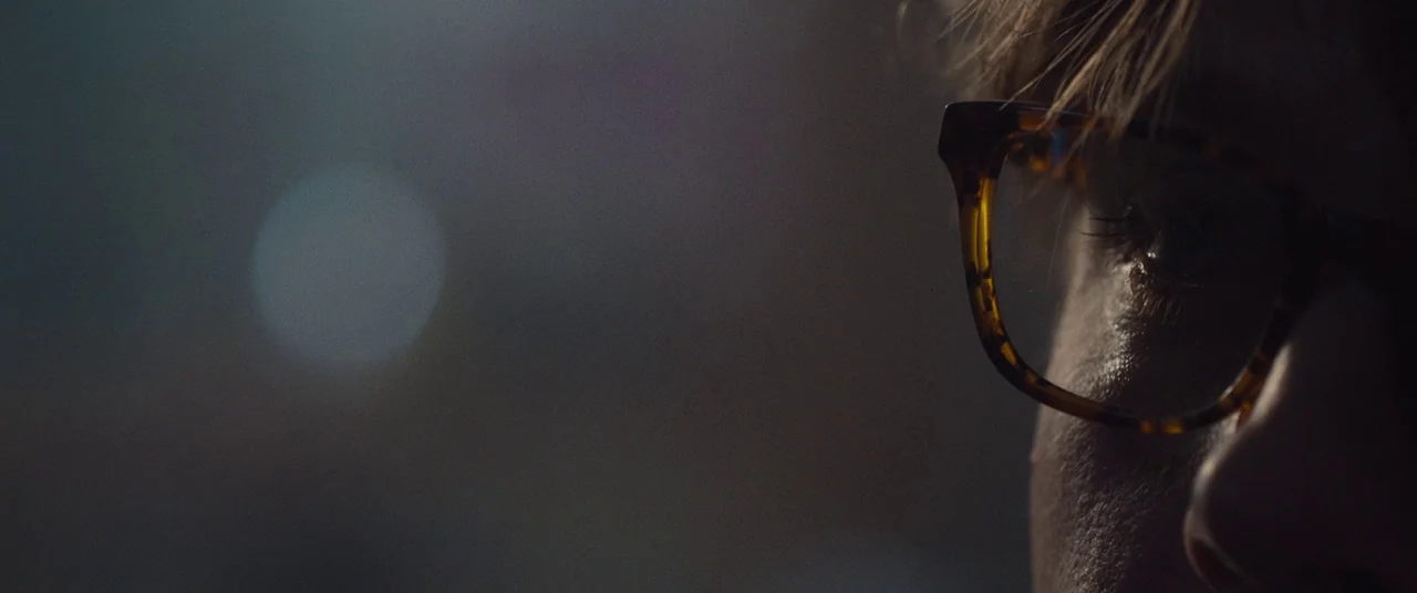 I Origins (2014) movie still: closeup — A dark environment with a soft out-of-focus light flare in the background. A person's profile is visible on…