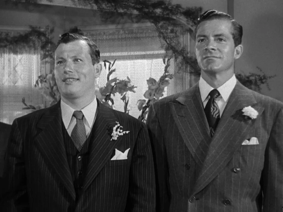 The Best Years of Our Lives (1946) movie still: medium — Two men stand together in front of a white curtain and floral display. They wear formal…