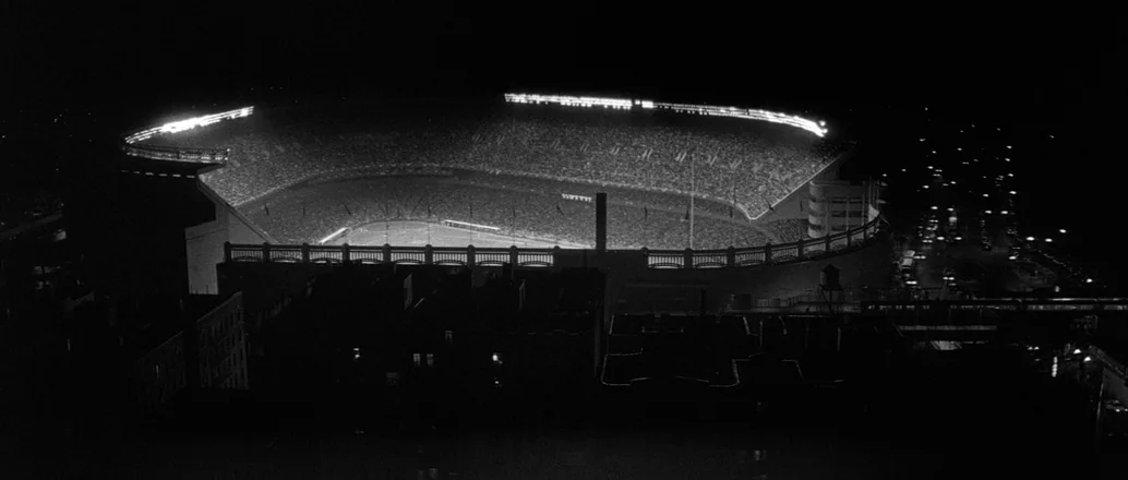 Manhattan (1979) movie still: establishing — A large urban stadium is illuminated by rows of bright floodlights at night. The surrounding dark city…