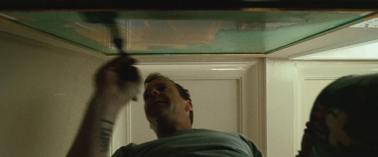 Mirrors (2008) movie still: medium — A man is shown from a low angle while working on a green horizontal surface. He holds a brush and appears to be…
