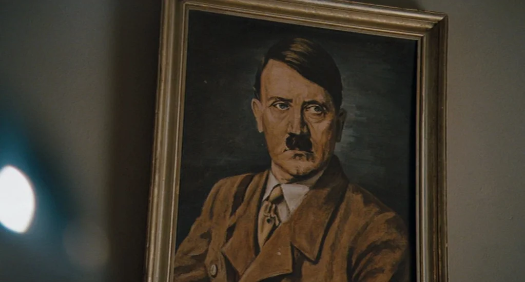 Valkyrie (2008) movie still: closeup — A framed portrait hangs on a plain, dark-painted wall inside a dimly lit room. The painting depicts an older…