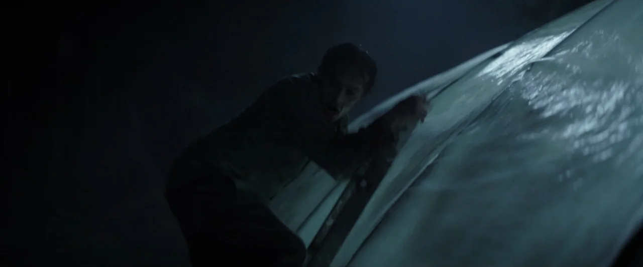Wolf Man (2025) movie still: medium — A dark night setting features a large canvas structure made of white material. A man climbs the steep side of…