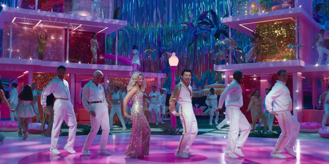 Barbie (2023) movie still: wide — A vibrant, plastic-like multi-level stage features metallic curtains and artificial palm trees. A group of…