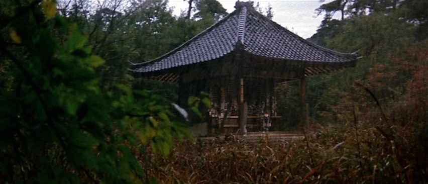 Lone Wolf and Cub: Baby Cart in Peril (1972) movie still: establishing — A traditional wooden pavilion with a dark tiled roof sits within a dense…