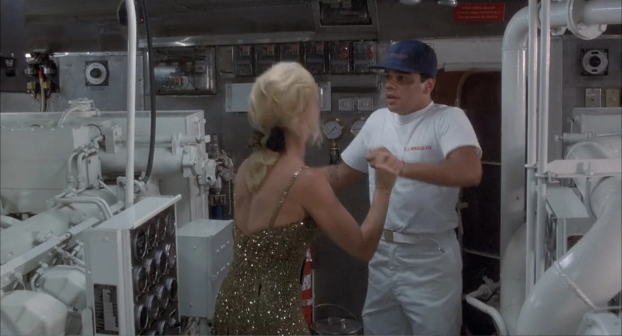 Overboard (1987) movie still: medium — A dense mechanical space with complex white piping and numerous gauges on metallic walls. A woman in a…