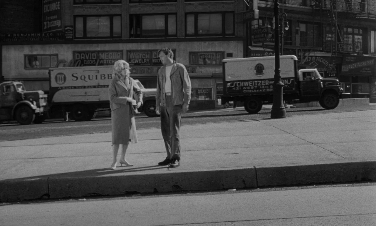Something Wild (1961) movie still: fullbody — A bustling city sidewalk features commercial buildings in the background with multiple delivery trucks…