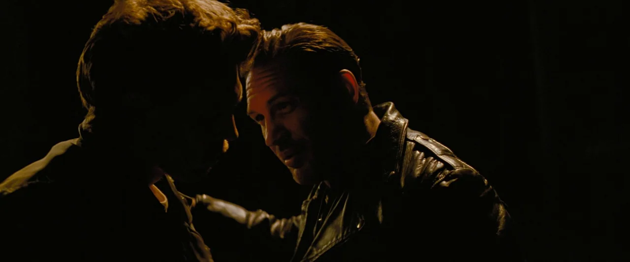 The Bikeriders (2023) movie still: medium — A dark, underexposed environment with no background details visible. Two men in black leather jackets…