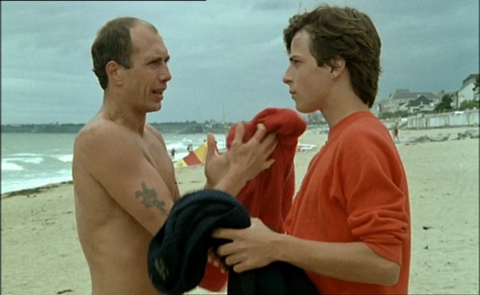Pauline At the Beach (Pauline à la plage) (1983) movie still: medium — A sandy beach stretches toward an overcast sea under a cloudy gray sky. Two…