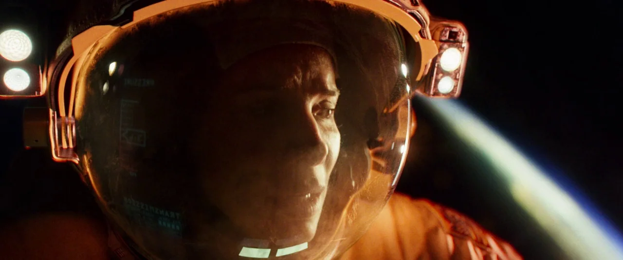 Gravity (2013) movie still: closeup — An astronaut in a spacesuit looks out from inside their clear helmet visor. The curved glass of the helmet…