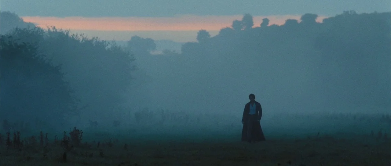 Pride & Prejudice (2005) movie still: wide — A sprawling, mist-covered field stretches toward distant trees under a pale dawn sky. A single man in a…