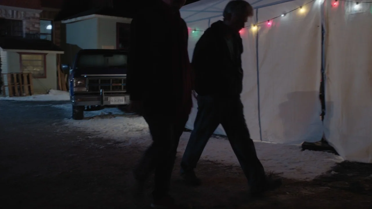 Designing Christmas (2022) movie still: fullbody — A snowy driveway at night features a white temporary tent decorated with lights. Two men walk…
