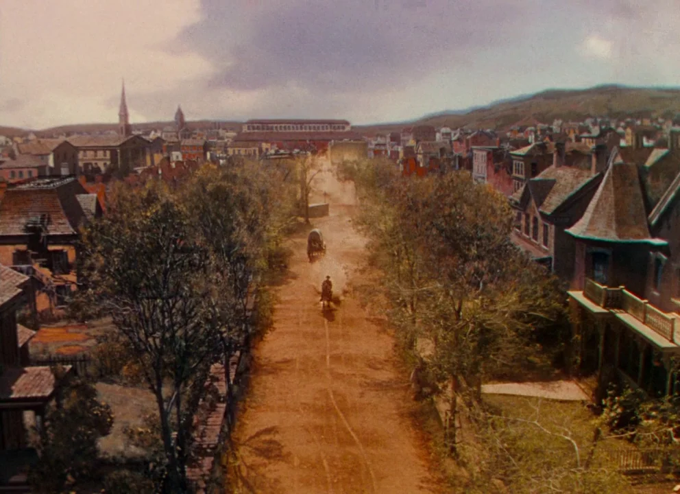 Gone with the Wind (1939) movie still: wide — A rural 19th-century town features a dirt road lined with trees and houses. A rider on horseback…